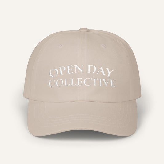 Beige cap with 'open day collective' text on a white background