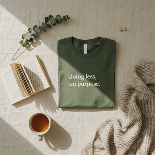 Dark gray t-shirt with 'doing less, on purpose' text on a light surface with accessories.