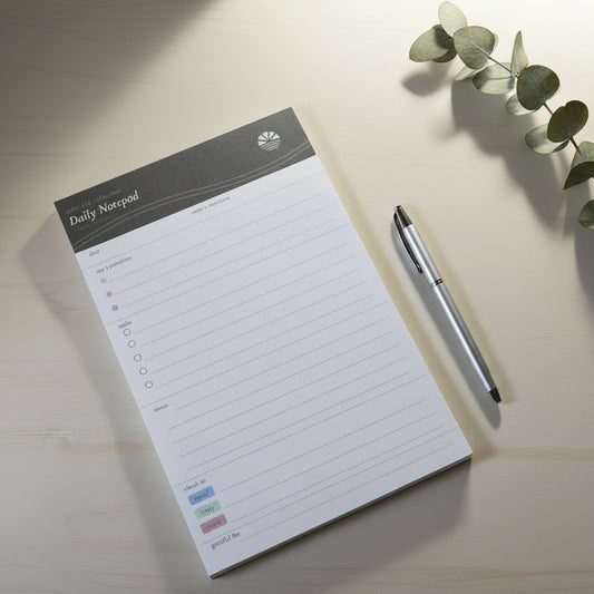 Daily notepad with a pen on a light surface with a plant
