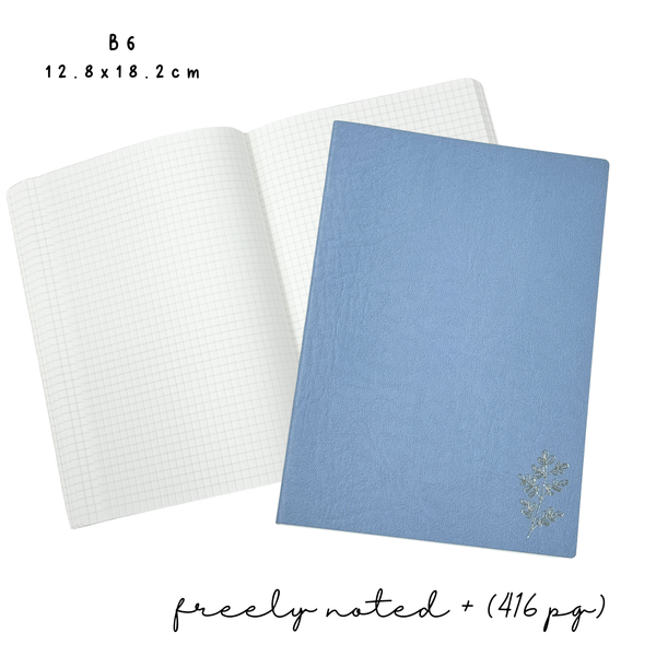 Two notebooks, one open showing white grid pages and one closed showing the blue with floral design cover, on a white background.