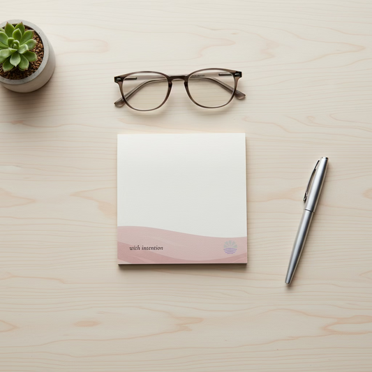 square post it with a dusty pink accent with the saying "with intention" on a light wood desk with minimal desk accessories around it